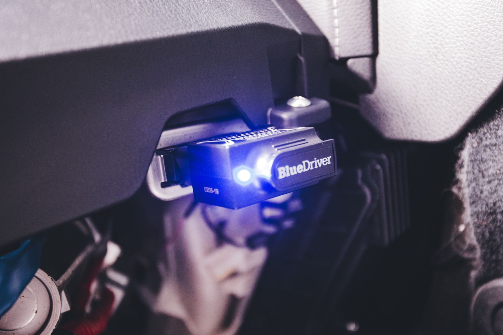 OBD-II Bluetooth scan tool plugged into a car's diagnostic port, glowing blue